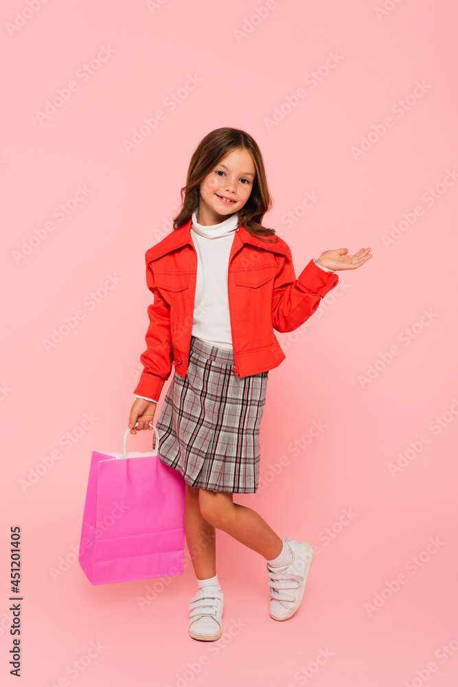 trendy girl with shopping bag pointing with hand while standing on pink trendy girl with shopping bag pointing with hand while standing on pink