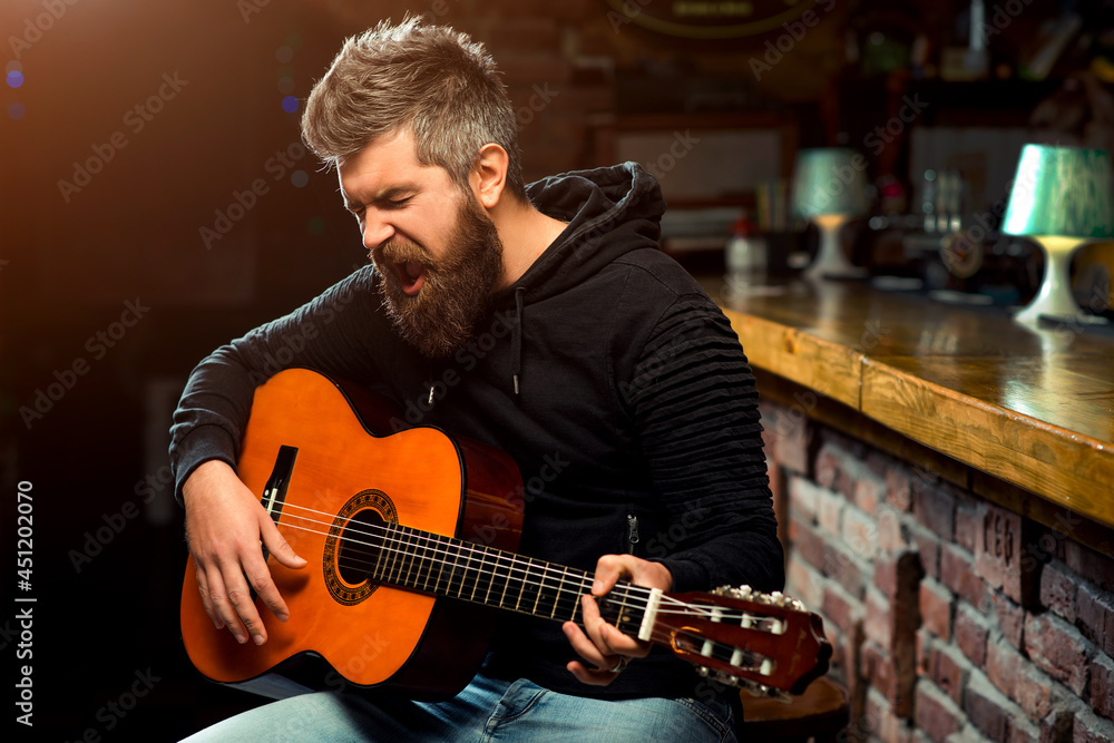 Fototapeta premium Handsome man with guitar singing songs at bar. Man play guitar in pub.