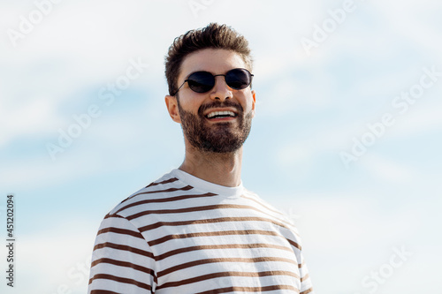 summer holidays and people concept - portrait of happy smiling young man in sunglasses over sky © Syda Productions