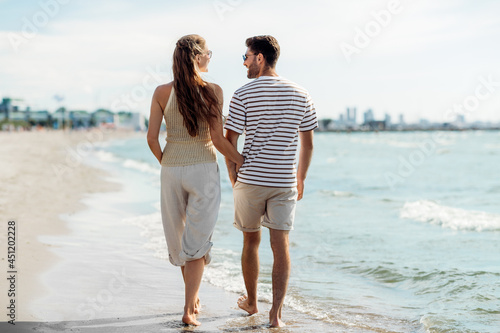 summer holidays and people concept - happy couple walking along beach in tallinn, estonia