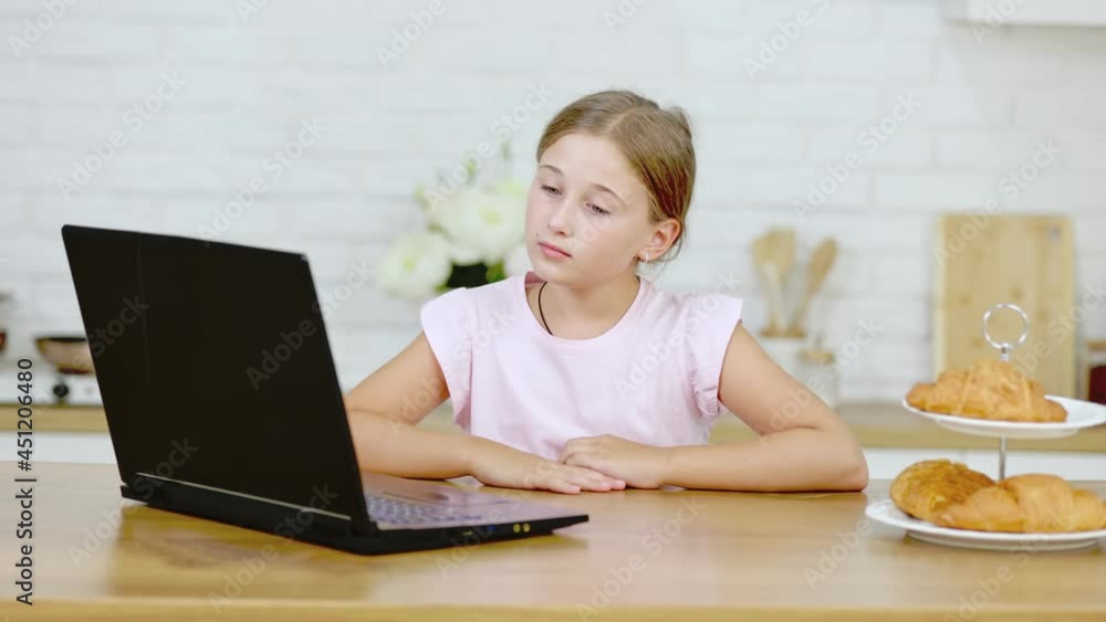 girl looking at a laptop sitting at the table in the kitchen girl looking at a laptop sitting at the table in the kitchen