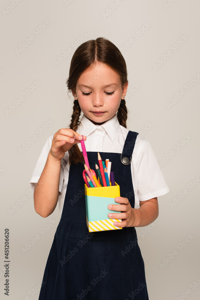 girl in school uniform taking felt pen from pen holder isolated on grey