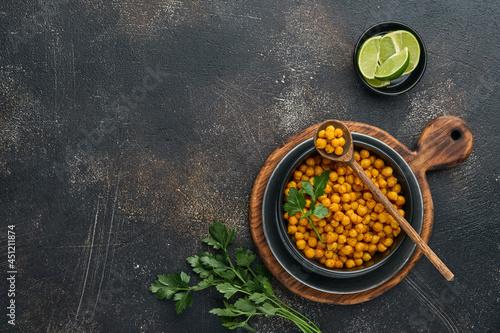 Fried chickpeas with turmeric with parsley and lime in black plate on an old black table background. Roasted spicy chickpeas or Indian chana or chole, popular snack recipe. Top view.