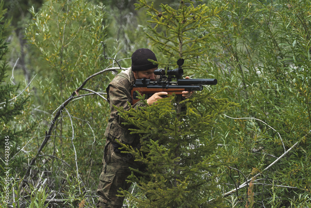 Fototapeta premium A man with a rifle sits in an ambush. The sniper is preparing to shoot.