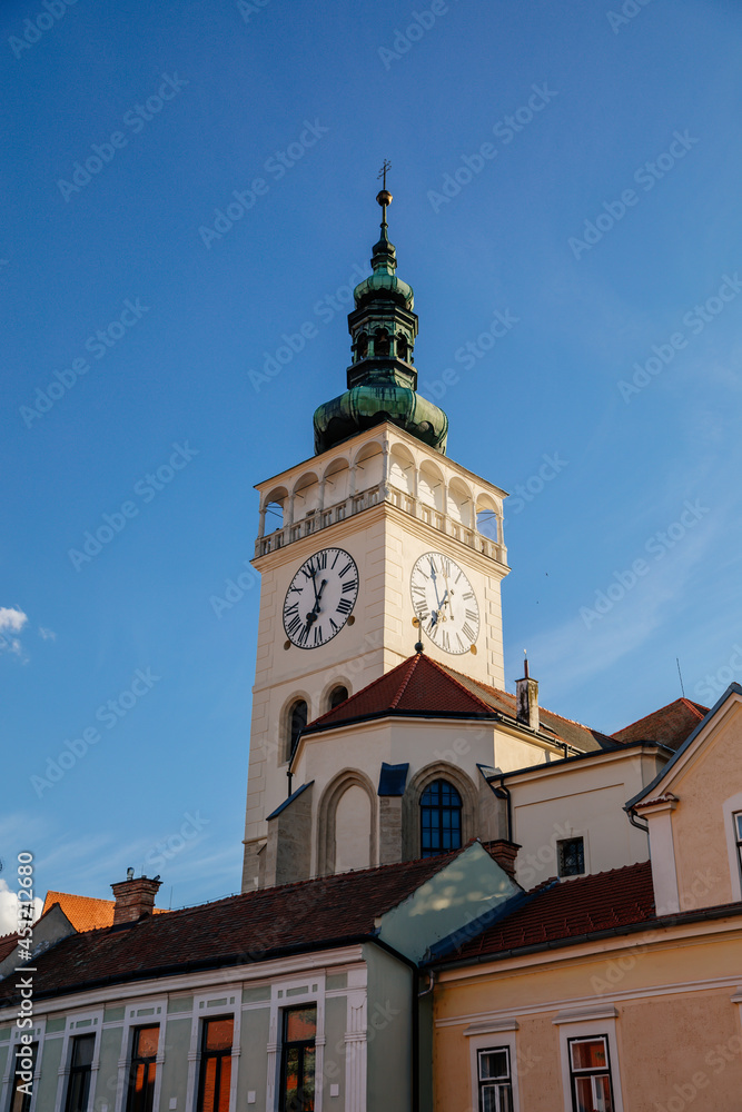 Mikulov, South Moravian Region, Czech Republic, 05 July 2021: medieval church square and white observation clock tower of St. Wenceslas church, green dome and red tile roofs at sunny summer day