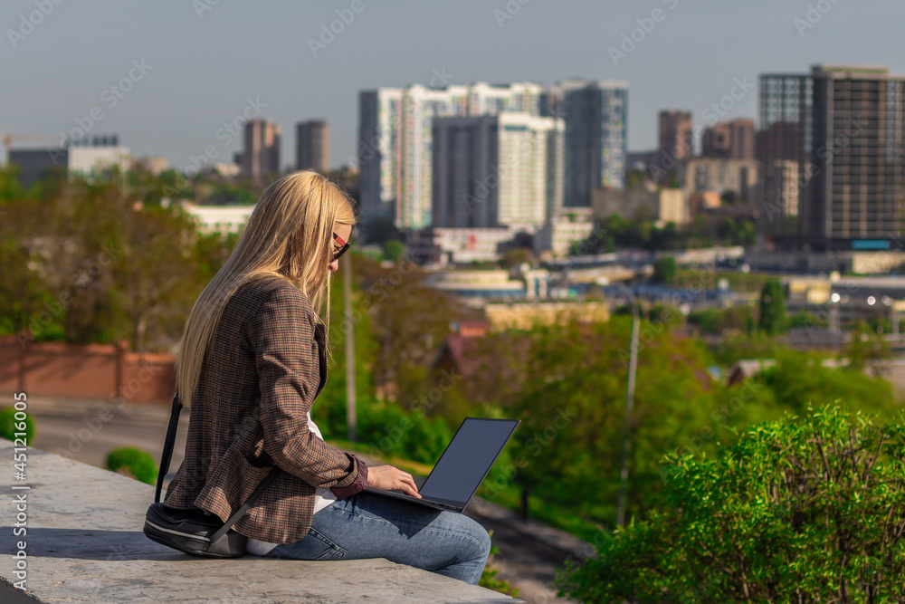 young blonde woman sits with her notebook against the background of the city young blonde woman sits with her notebook against the background of the city