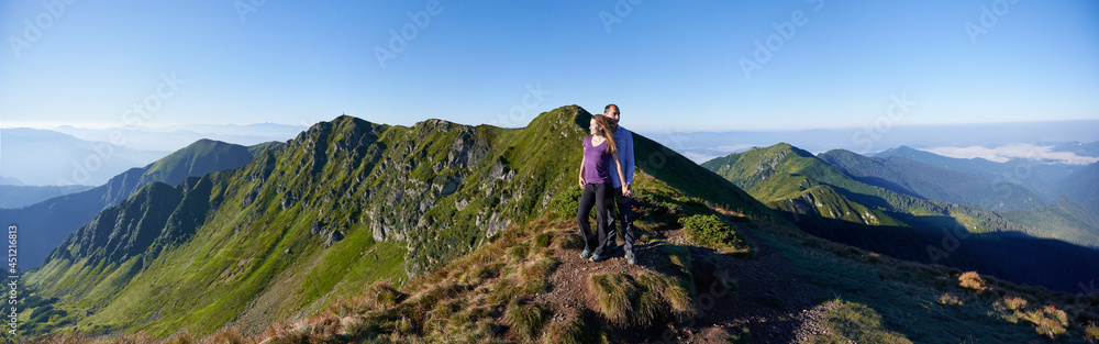 Couple on top of mountain. Woman and boyfriend are posing in the mountains and looking away. Concept of relaxation. Panoramic view Couple on top of mountain. Woman and boyfriend are posing in the mountains and looking away. Concept of relaxation. Panoramic view
