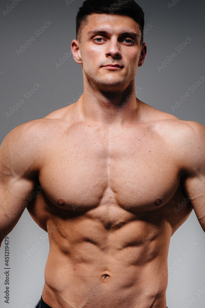 Fototapeta premium A young sexy athlete with perfect abs poses in the studio topless in jeans on the background. Healthy lifestyle, proper nutrition, training programs and nutrition for weight loss.