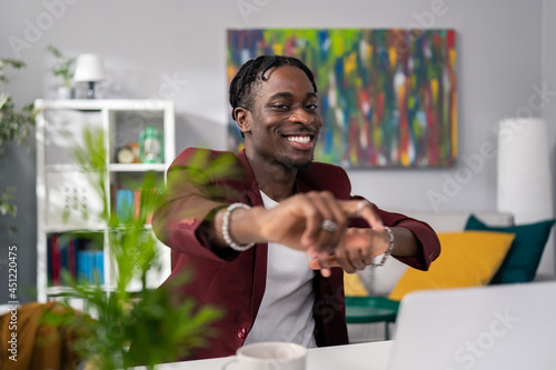 Elegant manager with dark skin businessman in jacket is satisfied with sold service products, happy with the monthly profits, sitting in front of computer victory dance, hands clenched into fists