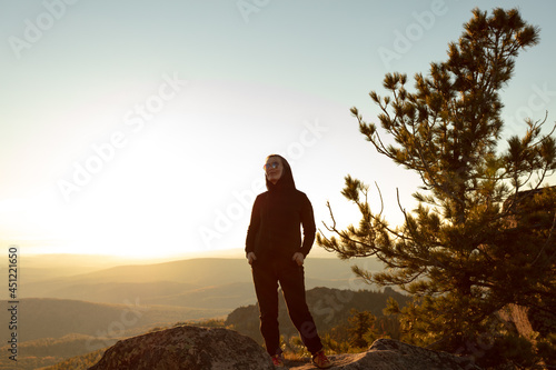 a tourist girl on the top of a cliff against the bright light from the sunset. mountain trekking  climbing  yoga in autumn or spring. active recreation. HIRES