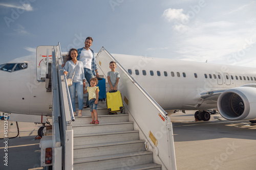 Happy family of four getting off the plane on a daytime. People, traveling, vacation concept