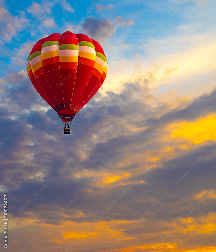 Fototapeta premium Red flying hot air balloon leisure activity against in the sunset sky. Happy and fun people in the basket in the sky