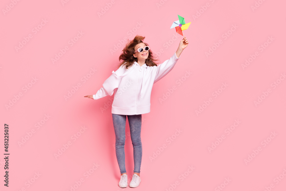 Full length body size girl wearing hoodie sunglass playing colored windmill isolated pastel pink color background Full length body size girl wearing hoodie sunglass playing colored windmill isolated pastel pink color background