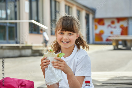 Lunch at school. A charming girl is eating breakfast, a snack at recess in the schoolyard. Nutrition for children from educational institutions photo