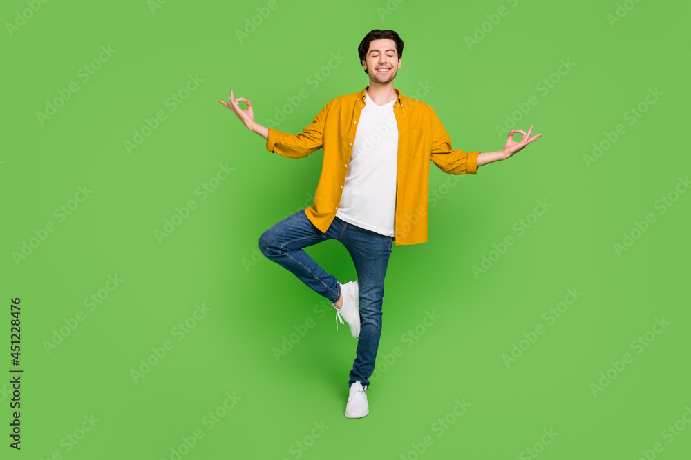 Full size photo of young funky smiling positive guy doing yoga relaxing free time isolated on green color background