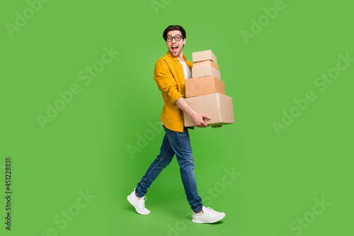 Full size photo of young handsome good mood man go walk hold carton boxes move new house isolated on green color background