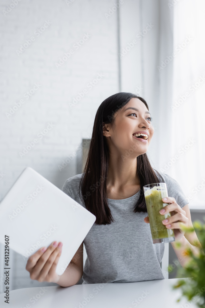 cheerful asian woman with glass of fresh smoothie and digital tablet laughing in kitchen. cheerful asian woman with glass of fresh smoothie and digital tablet laughing in kitchen.