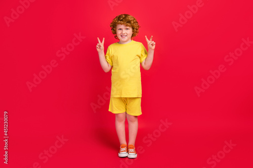 Photo of friendly positive little boy hands show two v-signs wear yellow t-shirt isolated red color background
