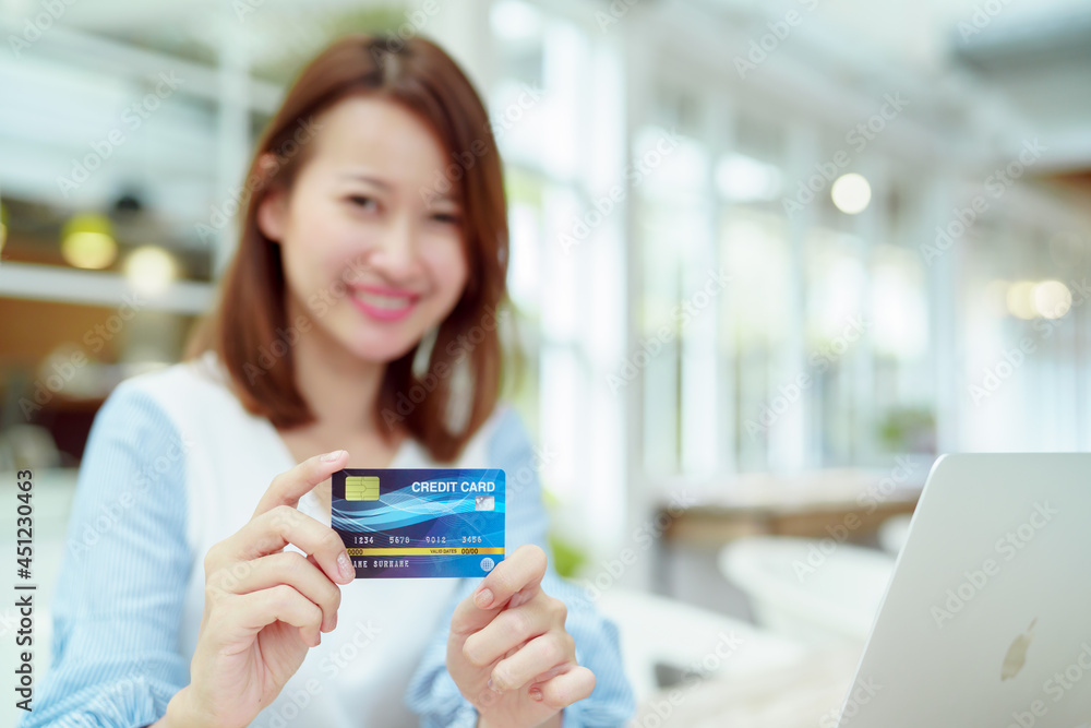 A credit card in a woman's hand with a background that is out of focus with an Asian woman in the background A credit card in a woman's hand with a background that is out of focus with an Asian woman in the background