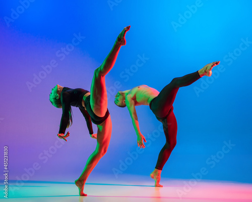 Stylish sportive caucasian couple, male and female dancer dancing contemporary dance on colorful gradient blue pink background in neon light.