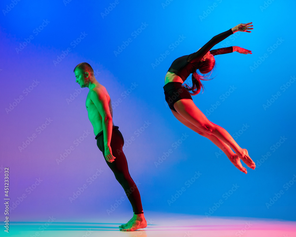 Stylish sportive caucasian couple, male and female dancer dancing contemporary dance on colorful gradient blue pink background in neon light.