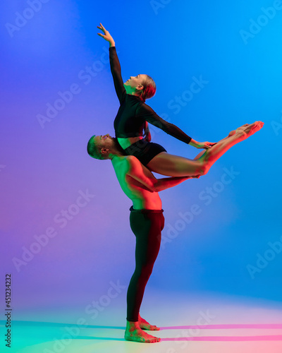 Stylish sportive caucasian couple, male and female dancer dancing contemporary dance on colorful gradient blue pink background in neon light.