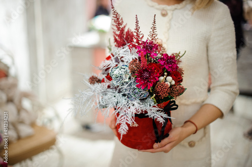 Close-up of box with flower arrangement in woman hands. Red and silver colors.