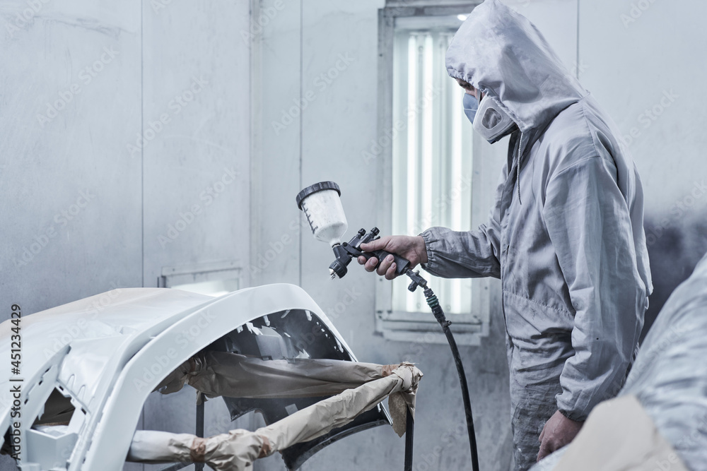 Car painting and automobile repair service. Auto mechanic in white overalls paints car with airbrush pulverizer in paint chamber. Car painting and automobile repair service. Auto mechanic in white overalls paints car with airbrush pulverizer in paint chamber.
