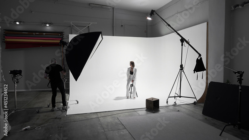 Fashion photography in a photo studio. Professional male photographer taking pictures of beautiful woman model on camera, backstage photo