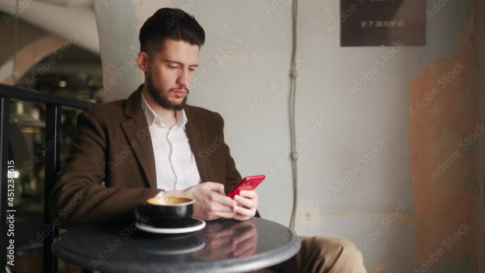 Classy young man using smartphone sitting in cafe. Guy browsing social network app in coffeshop. Office worker resting on break with a cup of coffee. Indoor scene. Classy young man using smartphone sitting in cafe. Guy browsing social network app in coffeshop. Office worker resting on break with a cup of coffee. Indoor scene.