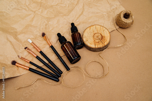 Cosmetic oil in a container with a pipette and makeup brushes lie on beige crumpled kraft paper.