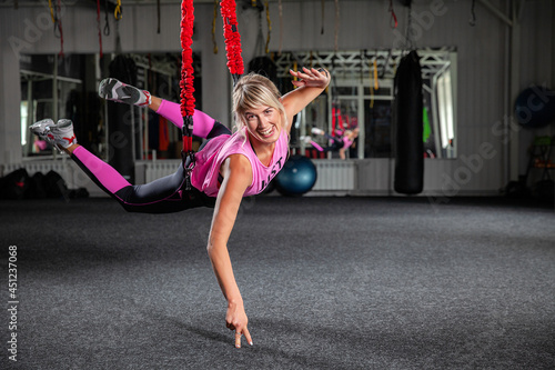 Bungee fitness. Training on loops. A beautiful sports woman in a pink tracksuit trains in the gym with the help of special loops. Poses in limbo