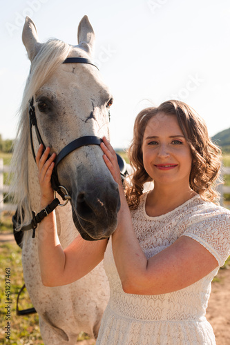 Portrait of a young woman in a dress hugging horse