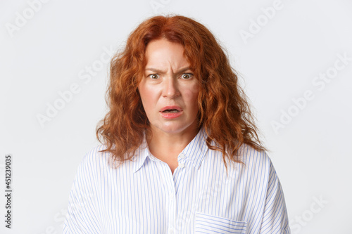 People, emotions and lifestyle concept. Close-up of frustrated and displeased middle-aged woman cringe from something disgusting and confusing, standing white background