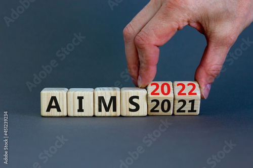 Business concept of planning 2022 aims new year. Businessman turns a wooden cube and changes words 'Aims 2021' to 'Aims 2022'. Beautiful grey background, copy space. Business, 2022 aims concept.