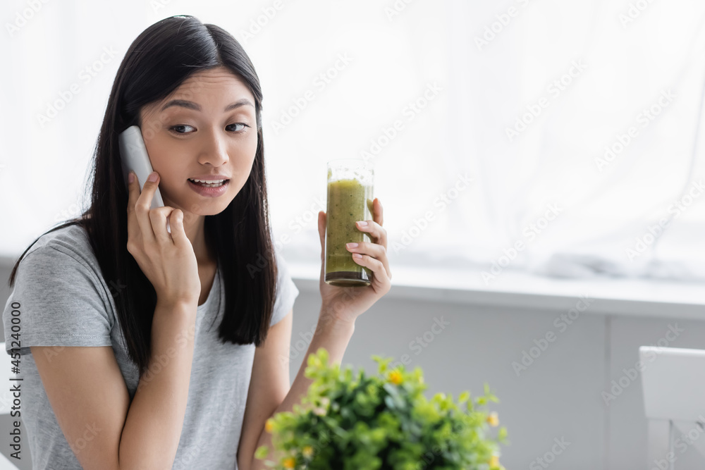 young asian woman calling on mobile phone while holding glass of smoothie near blurred plant. young asian woman calling on mobile phone while holding glass of smoothie near blurred plant.