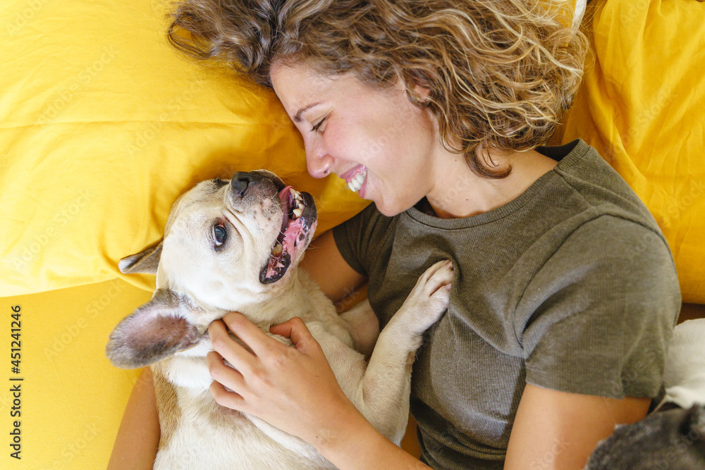 Woman dog lover with bulldog in bed. Top view of woman playing with pet. Lifestyle with animals indoors.