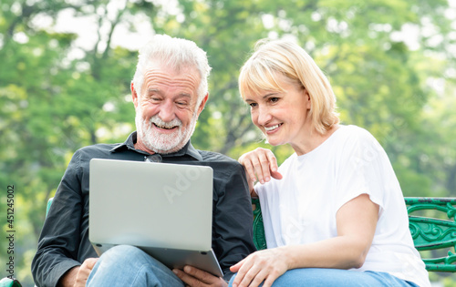 computer together while sitting on bench outdoors. Cheerful retirement keeping smile on his face while checking his counting. 