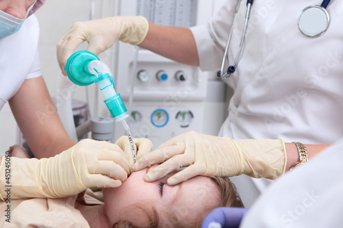 Little girl before surgery. Resuscitator holds an oxygen mask on the child's face. General anesthesia. Life saving. Artificial lung ventilation apparatus.