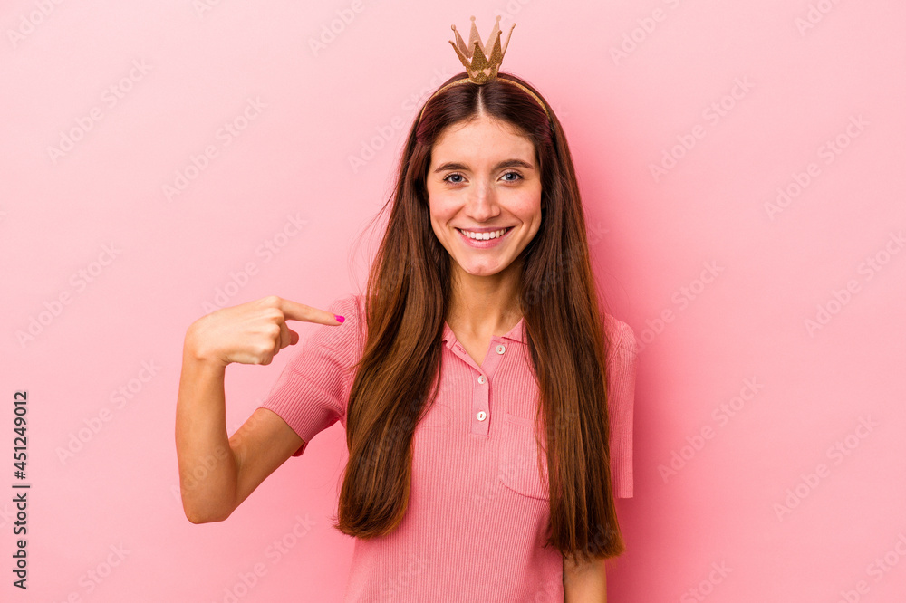 Young caucasian woman wearing crown isolated on pink background person pointing by hand to a shirt copy space, proud and confident Young caucasian woman wearing crown isolated on pink background person pointing by hand to a shirt copy space, proud and confident