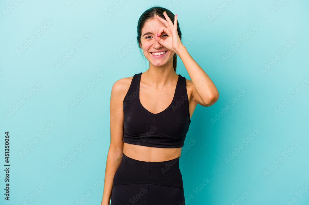 Young sporty caucasian woman isolated on blue background excited keeping ok gesture on eye.
