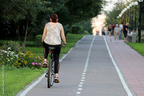 Woman in sports leggings riding on a bicycle on a path in a green park. Girl cyclist, summer leisure, cycling concept