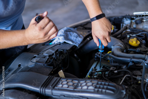 Auto mechanic working and repairing a car engine in a garage with a screwdriver and a torch. photo
