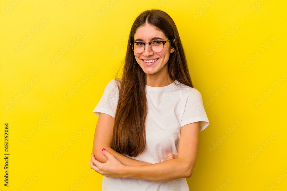 Young caucasian woman isolated on yellow background who feels confident, crossing arms with determination. Young caucasian woman isolated on yellow background who feels confident, crossing arms with determination.