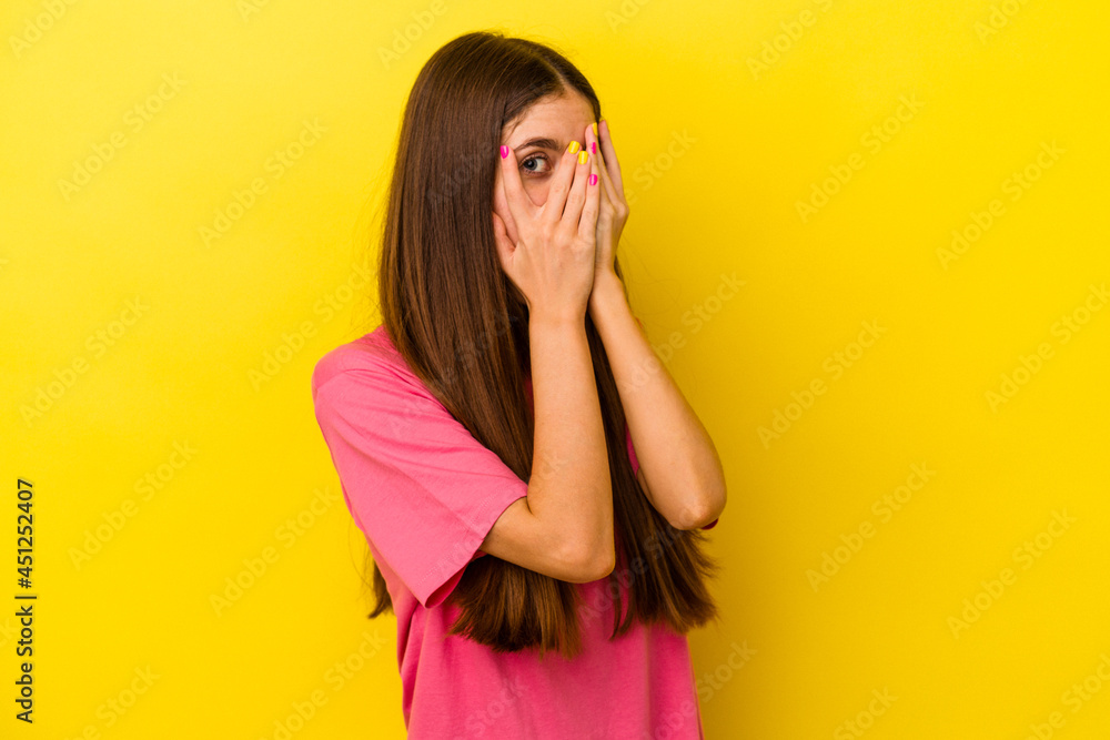 Young caucasian woman isolated on yellow background blink through fingers frightened and nervous. Young caucasian woman isolated on yellow background blink through fingers frightened and nervous.