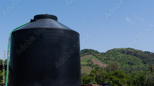 tinaco de agua negro en azotea de casa rural con cerros al fondo