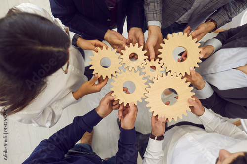 Overhead view on diverse business team people hands holding gear wheels finding working solutions. Power partnership, engineering teamwork, manage team work and company activities concept photo
