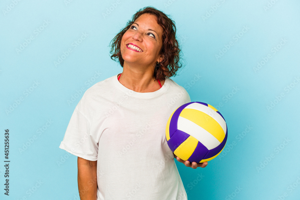 Middle age latin woman playing volleyball isolated on blue background dreaming of achieving goals and purposes