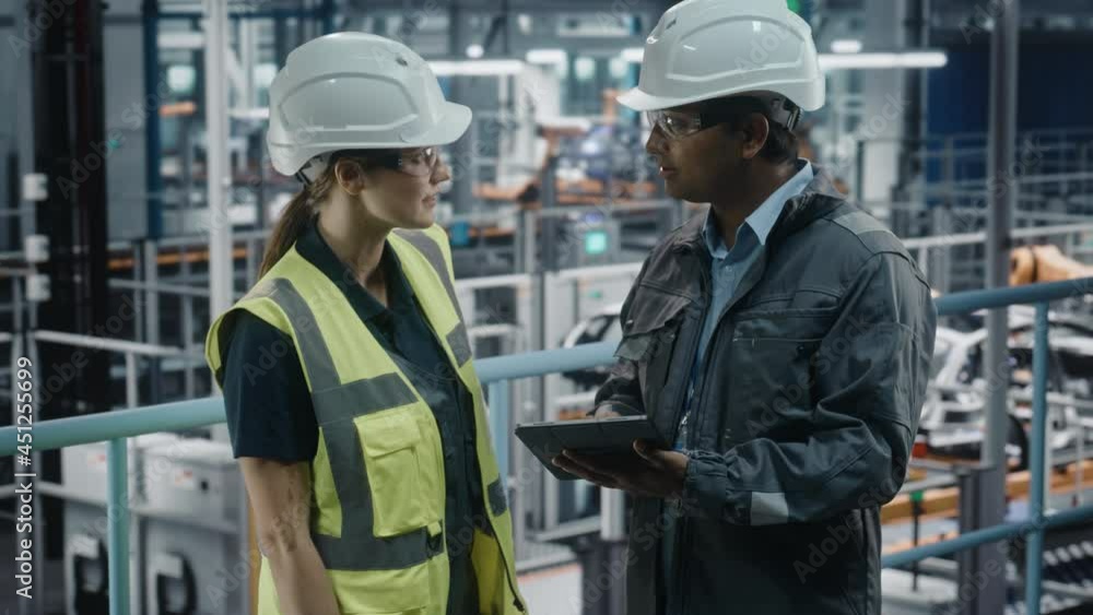 Male Specialist and Female Car Factory Engineer in High Visibility Vests Using Tablet Computer. Automotive Industrial Manufacturing Facility Working on Vehicle Production. Diversity on Assembly Plant. Male Specialist and Female Car Factory Engineer in High Visibility Vests Using Tablet Computer. Automotive Industrial Manufacturing Facility Working on Vehicle Production. Diversity on Assembly Plant.