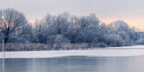 Winter view with snow-covered trees on the shore river in the morning during sunrise © Volodymyr